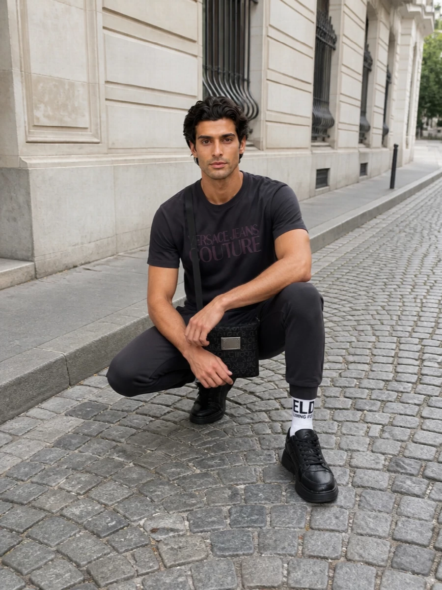 Charcoal and black keep this Versace tee front and centre, paired with tapered Dsquared2 joggers for a clean, athletic base. Giuseppe Zanotti sneakers and a structured Dolce&Gabbana crossbody sharpen the streetwear mood while staying easy for all-day city wear. Logo socks are the quiet finishing touch, reinforcing the graphic theme without disrupting the muted palette.