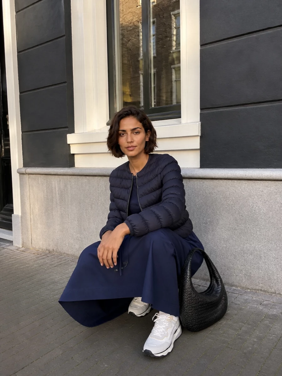 I am building around the dress path here, letting the navy technical midi act as a single, continuous column under the cropped puffer rather than breaking the line with separate top and trousers. The result is a quiet sport-luxe city outfit: deep navy layers, soft white sneakers and a sculpted black shoulder bag that keeps everything polished without tipping formal. It is the kind of combination that moves easily from daytime errands to relaxed dinners just by changing jewellery or lip colour.