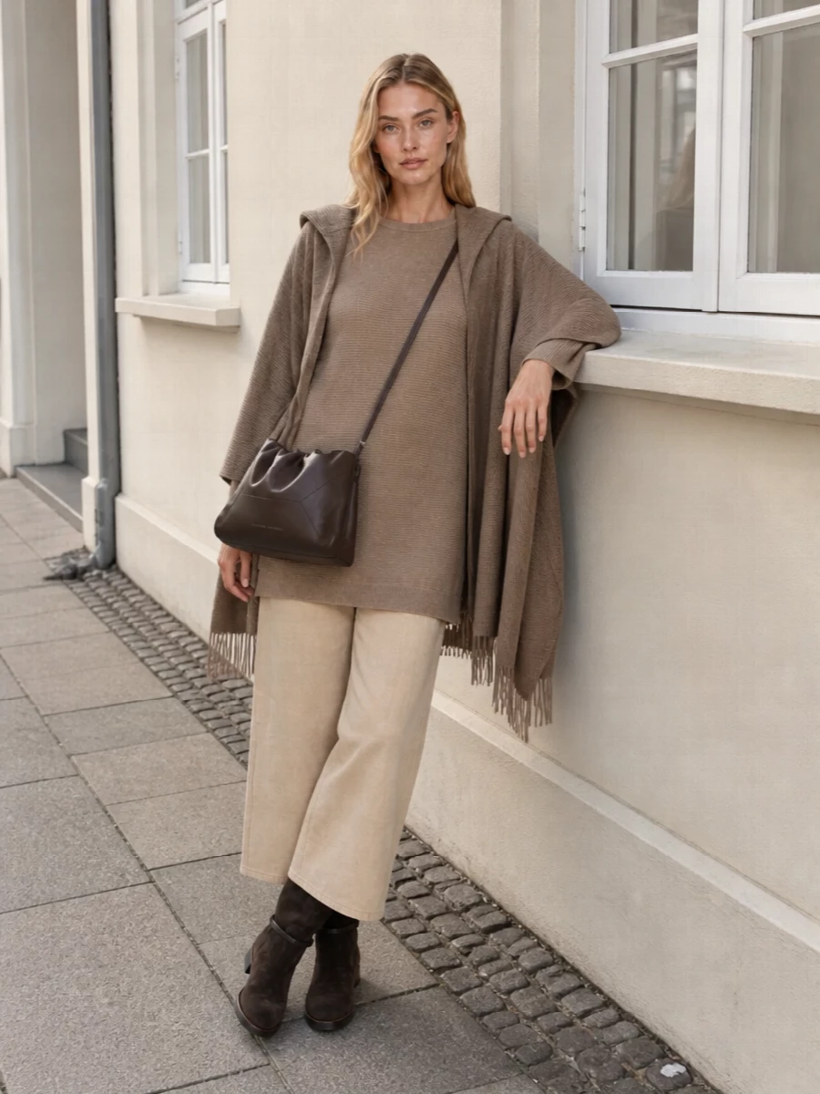 A long camel ribbed knit paired with light beige wide-leg trousers creates a soft, elongated column in tonal neutrals. Dark espresso knee boots and a chocolate crossbody sharpen the palette just enough, keeping the mood relaxed yet city-ready. The result is a quietly luxurious ensemble suited to travel days, off-duty errands, or muted lunches alike.