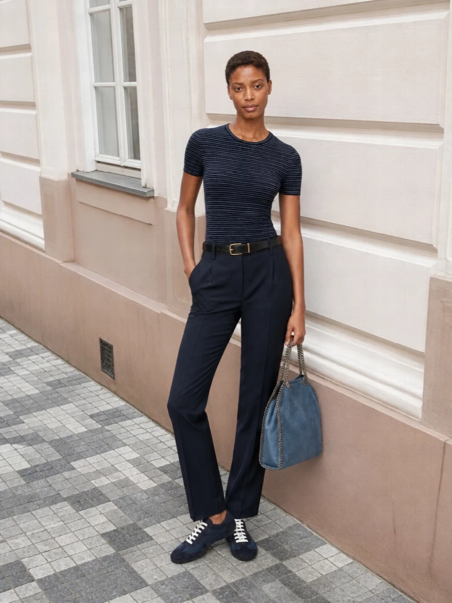 This look leans into a navy-on-navy, quietly tailored narrative: the slim striped knit is grounded by precise pinstriped trousers for a long, refined silhouette that still feels effortless. Inky mesh sneakers keep the mood relaxed yet luxe, while the slate-blue tote introduces a soft tonal contrast that maintains the minimalist, polished feel for everyday city dressing or a modern office.