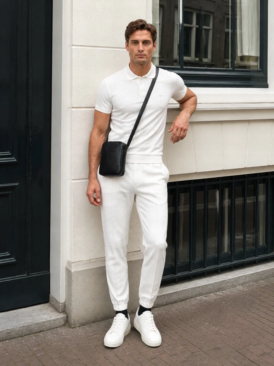 Soft white joggers and a matching Emporio Armani polo create a clean, modern take on relaxed sport tailoring. Creamy off-white sneakers keep the line streamlined, while a slim black leather crossbody and matching socks add just enough contrast for city days or travel. The result is quietly confident, minimal and easy to wear from brunch to airport lounge.