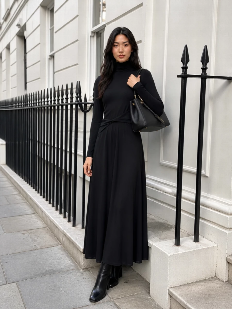 An inky Fabiana Filippi column dress pairs with the structured Emporio Armani tote for a quietly luxurious, all-black evening ensemble. The long, fluid silhouette balances covered shoulders and a defined waist, keeping the mood polished rather than overt. Sleek Hogan ankle boots ground the length with a modern, city-ready finish that still feels refined beside the bag’s gold hardware.