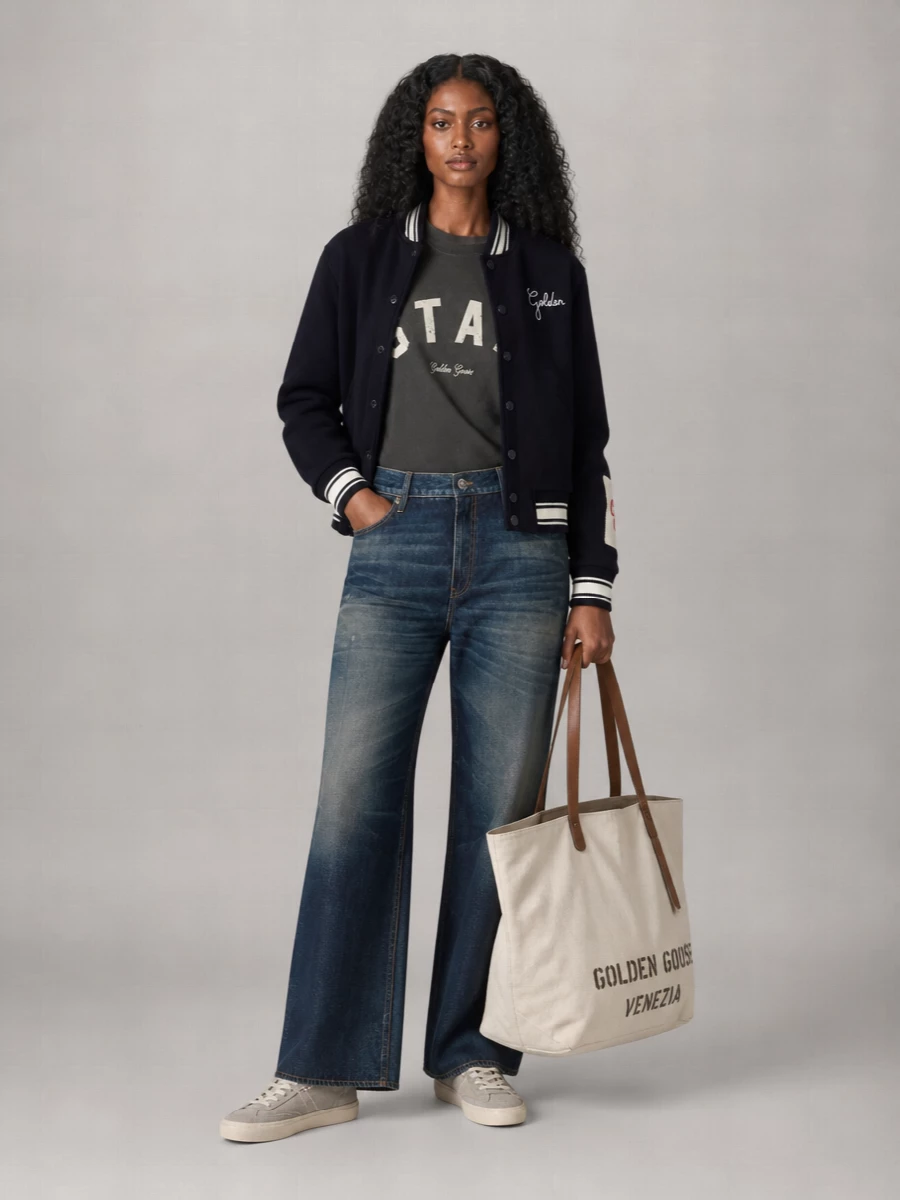 I’m building around the varsity bomber with a clean, sport-street base instead of competing sequins or dressy pieces. The charcoal collegiate tee and wide-leg jeans keep the palette grounded in navy, grey, and cream, so the jacket reads intentional rather than costume. Lived-in Golden Goose sneakers and the canvas tote finish it with that easy, city-ready nonchalance you actually want to run around in all day.