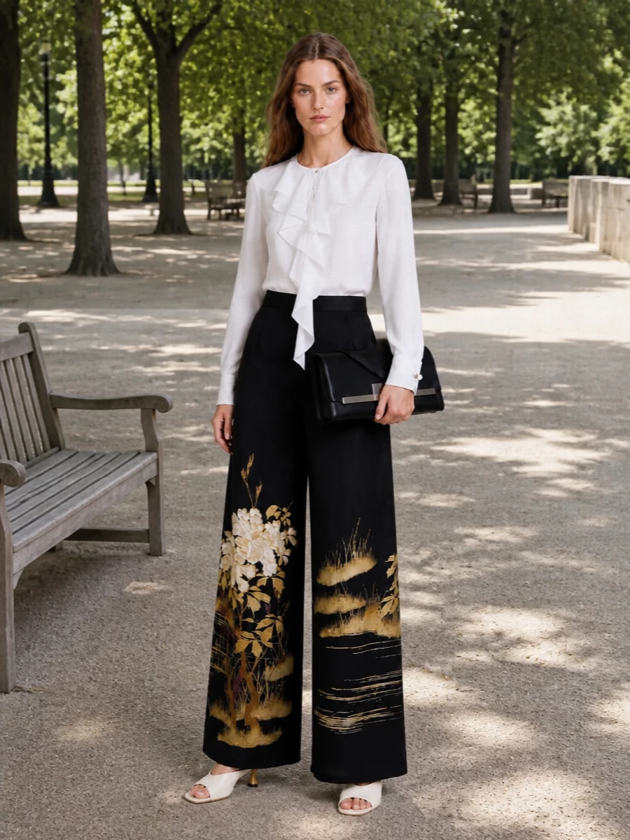 A fluid black embroidered trouser is paired with a white ruffled blouse for a romantic yet precise evening ensemble. Ivory and gold accents stay close to the body, while the black clutch quietly anchors the drama. The result is formal, modern occasionwear that feels rich and composed rather than overtly decorative.