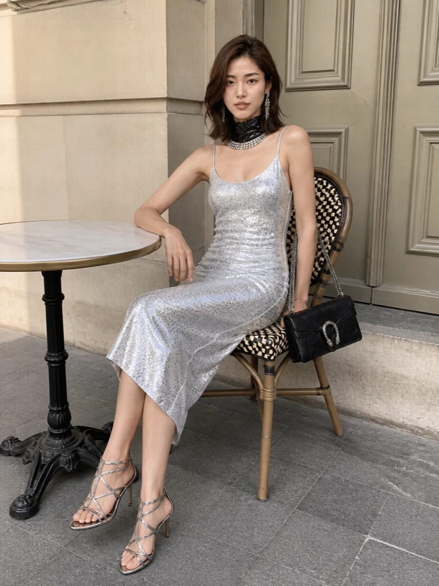 A column of silver catches the light, grounded by black and chrome details that feel sharp rather than sugary. Strappy metallic heels, a structured Gucci shoulder bag and liquid-like jewelry keep everything in a tight, nocturnal palette. The result is pure late-night polish, made for rooms where the dress and the light do most of the work.