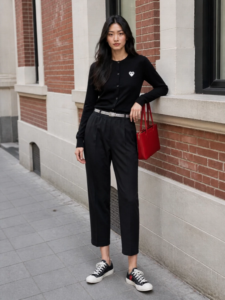 Black Play knit, cropped tailored trouser and low-top sneakers create a clean, graphic take on casual city dressing. The slim silver belt and cherry-red mini tote add just enough structure and color to keep it sharp and intentional without losing the ease.