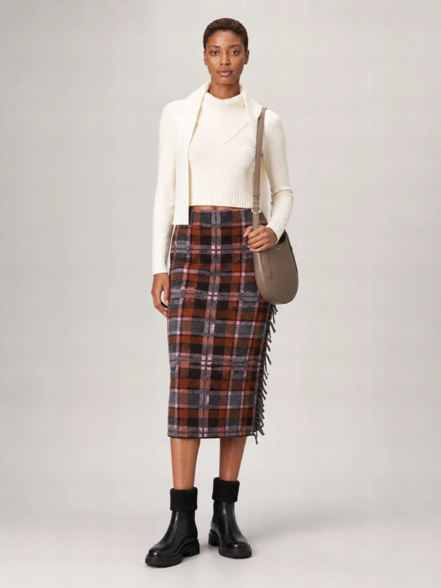 An ivory cropped knit sits neatly over a rust and charcoal plaid midi, letting the high waist and fringe detail carry the preppy focus. Chunky black ankle boots and a curved taupe cross-body keep the palette grounded and polished, ideal for city days when you want warmth with quiet structure. The slim ivory neckerchief finishes the neckline with a soft architectural touch that stays firmly in the minimalist mood.
