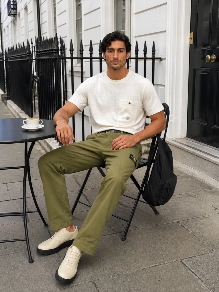 Stone Island’s olive straight leg is pared back with an off white pocket tee, giving a clean utility base that still feels relaxed. Cream and sand runners keep the line streamlined and light, while a black technical backpack and slim belt sharpen the city-ready attitude without fighting the muted palette. The result is an easy warm weather uniform that reads modern, functional and quietly branded.