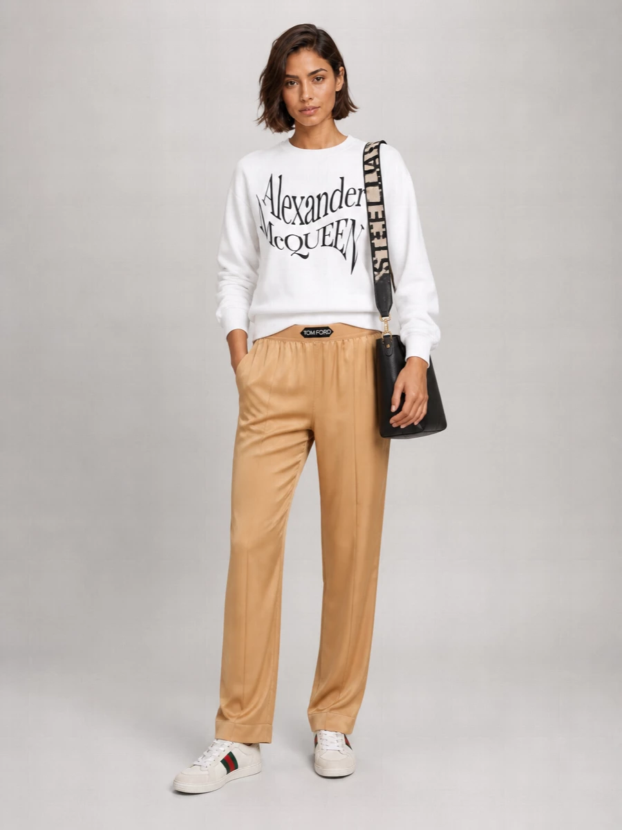 This is a sport-inflected city outfit that treats the Gucci low-tops as the anchor, pairing them with a crisp McQueen logo sweatshirt and fluid Tom Ford track pants. The camel and white palette keeps everything calm around the sneaker’s green and red stripe, reading polished enough for daytime while still feeling like true off-duty luxury. Choosing separates over a dress lets the whole set lean into athletic ease without losing that designer sharpness.