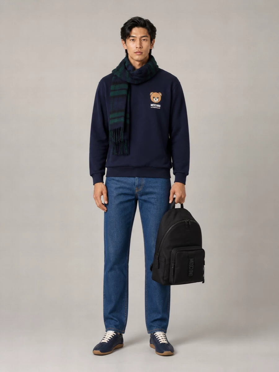 A navy teddy sweatshirt meets clean straight-leg indigo denim for a polished, off-duty Moschino uniform. Navy leather sneakers and a tonal tartan scarf keep the palette tight, while the black logo backpack adds practical street energy without shouting. It is relaxed enough for weekend city laps yet considered enough for casual meetups.