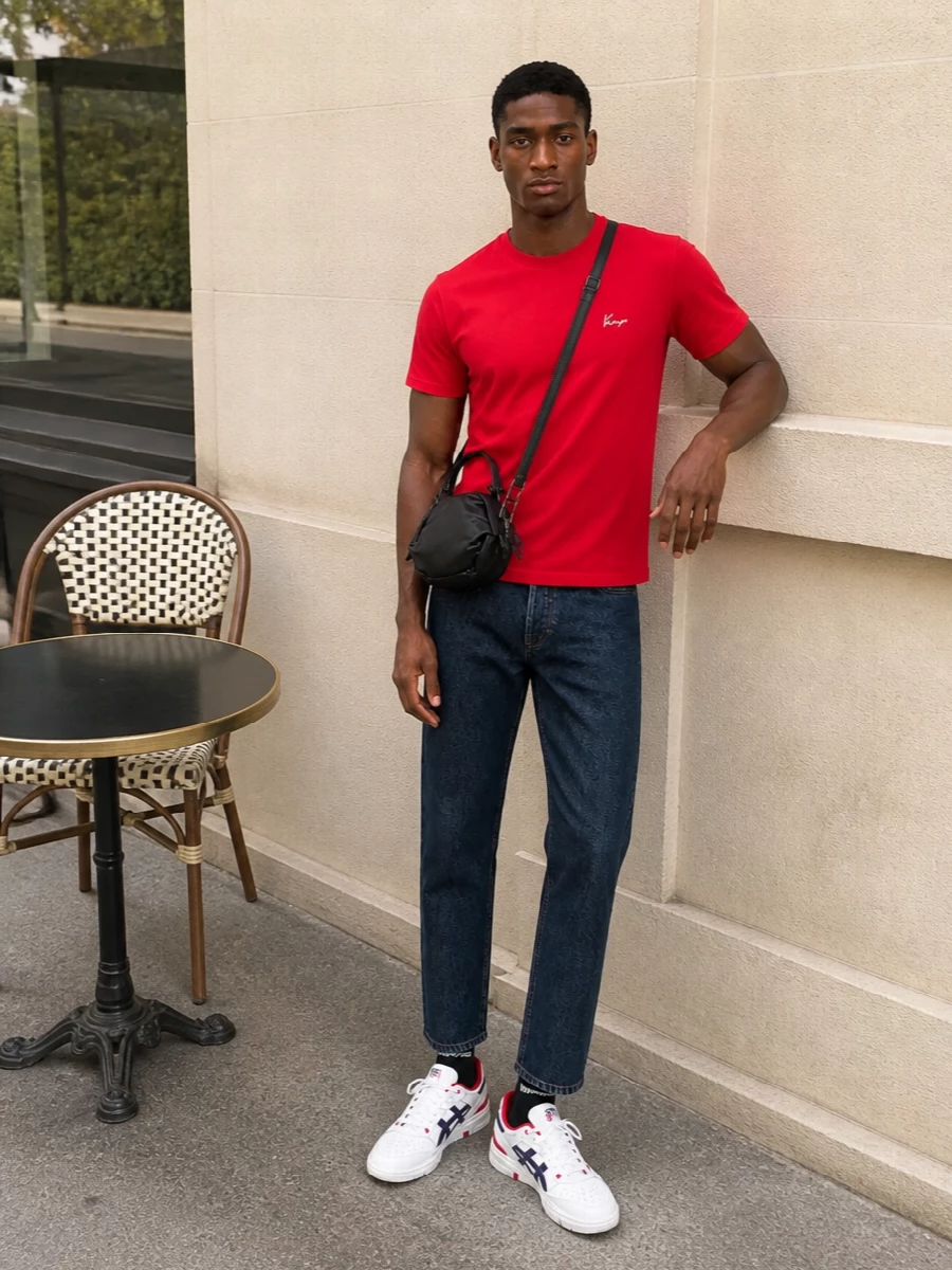 A clean red Kenzo tee sits over dark indigo denim for a simple, confident base that feels graphic without trying too hard. White court sneakers with navy and red hits echo the palette and keep the energy sporty, while a compact black crossbody and logo socks finish things with just enough street detail. It is an easy, city-ready uniform that stays sharp from day errands to low-key nights out.