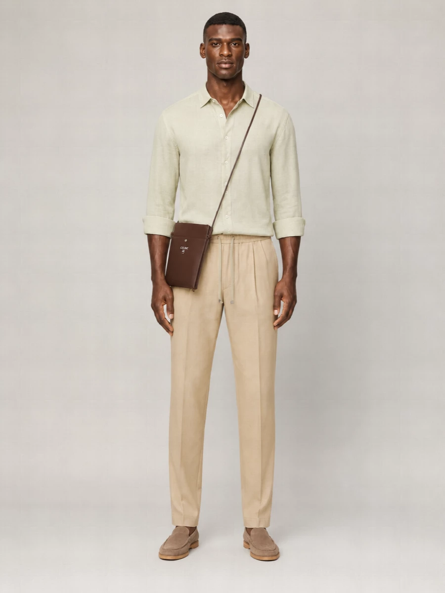 Sand drawstring tailoring with a muted sage linen shirt keeps the palette soft and tonal, reading relaxed yet considered. Taupe suede loafers and a camel belt sharpen the finish without breaking the ease, while the chocolate crossbody adds depth and a discreet note of polish for city days or travel.