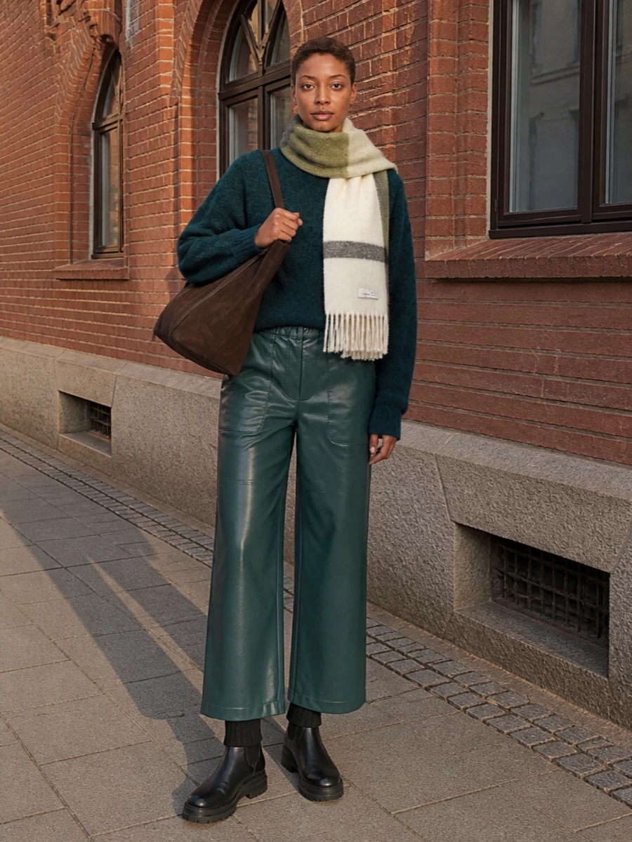 Deep teal and forest green sit in the same lush spectrum here, so the oversized knit and leather trouser read as a single, modern column. Chunky black boots and a sculptural chocolate tote ground the volume and keep the mood low-key, city-ready. The brushed scarf quietly ties the palette together, adding warmth without breaking the minimalist line.