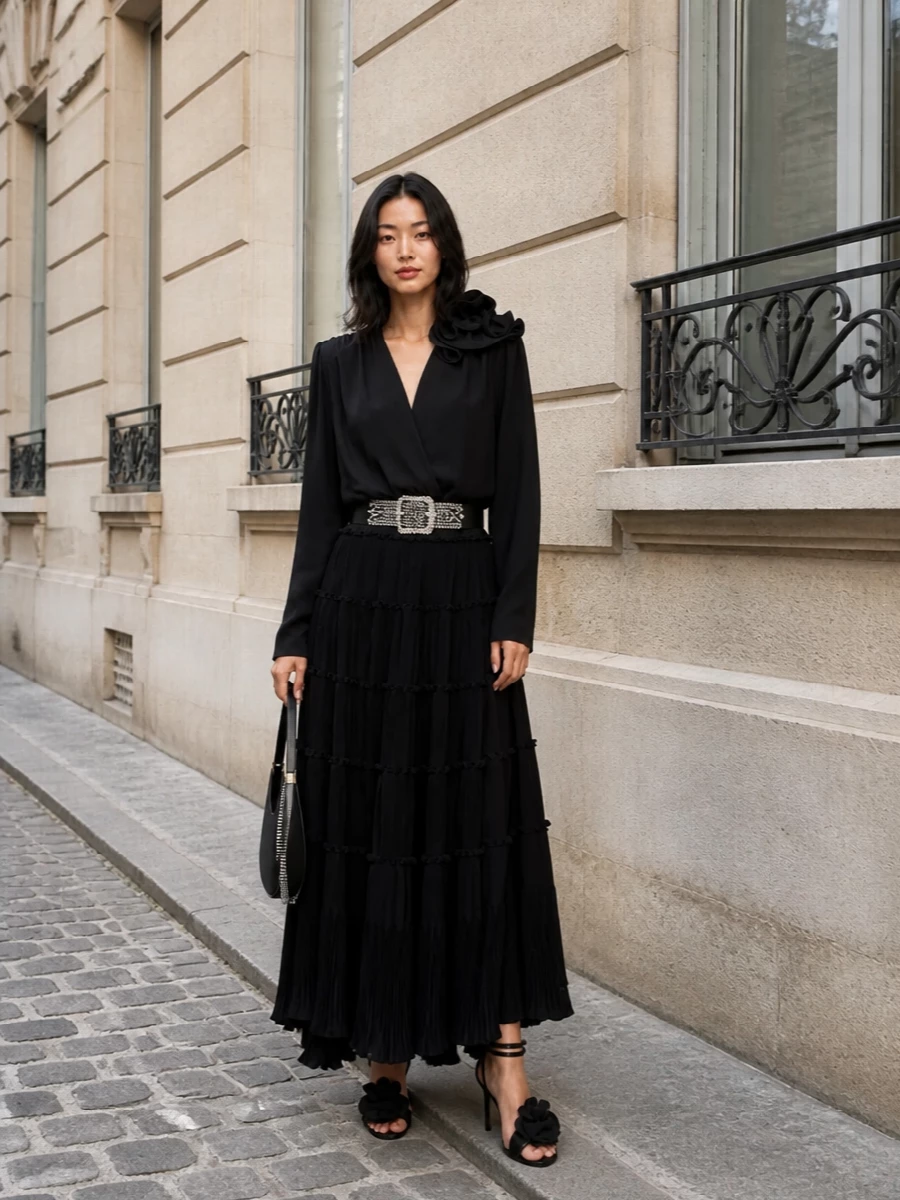 A study in nocturnal romance, this pairing lets the tiered black maxi skirt move like liquid while a sculpted, floral-draped blouse frames the shoulders. A crystal belt and strappy rose-detailed sandals draw the eye along the length of the body, with a sleek crescent bag as the final, restrained glint of metal. Everything stays inky and textural, so the drama comes from movement and silhouette rather than loud color.