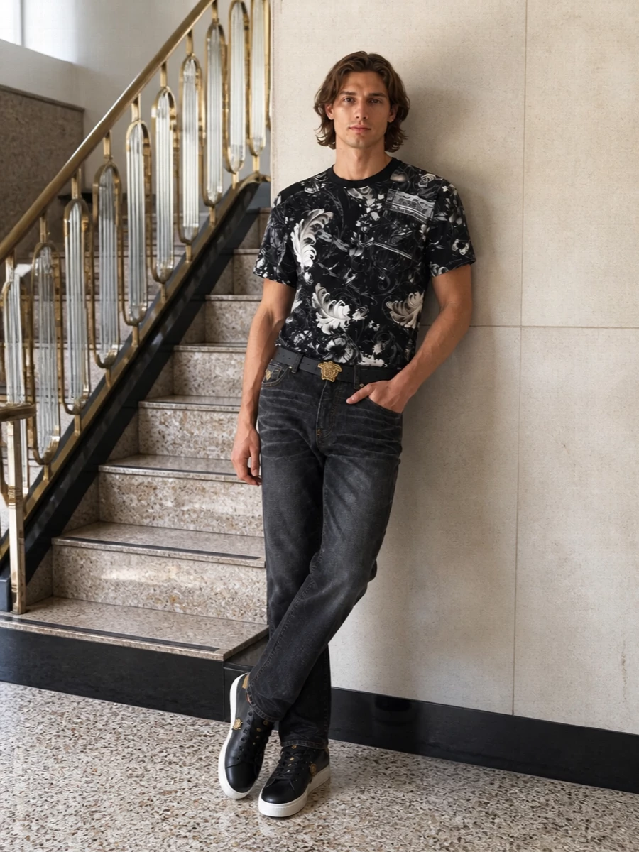 A monochrome Versace story built around the baroque tee, grounded with washed-black straight-leg denim for a sharp, downtown line. Black and gold sneakers keep the mood graphic yet wearable, while the Medusa belt and streamlined backpack pull the branding into a focused, street-ready finish.