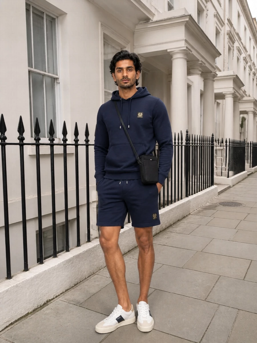 A navy-on-navy Belstaff base keeps this relaxed hoodie-and-short combination sharp rather than sloppy, with the tonal set reading clean and considered. Off white court-style sneakers break up the depth with a bright hit that still feels sporty, while the slim black crossbody adds just enough function for city days without cluttering the lines. It is an easy off duty uniform that moves from coffee runs to weekend walks with zero effort required from you.