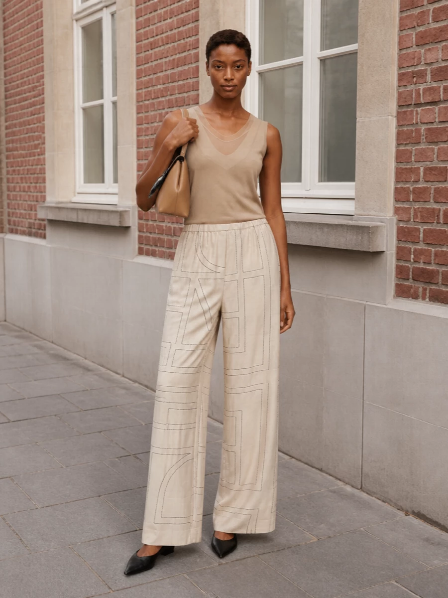 Warm neutrals and precise lines create a soft but assured Totême uniform here, with the graphic pant and layered tank reading as one continuous, sculpted column. Black leather accessories introduce just enough contrast to keep the palette from feeling too gentle, while the camel bag quietly echoes the base tones. It is relaxed, city ready and quietly confident from morning errands to late casual dinners.