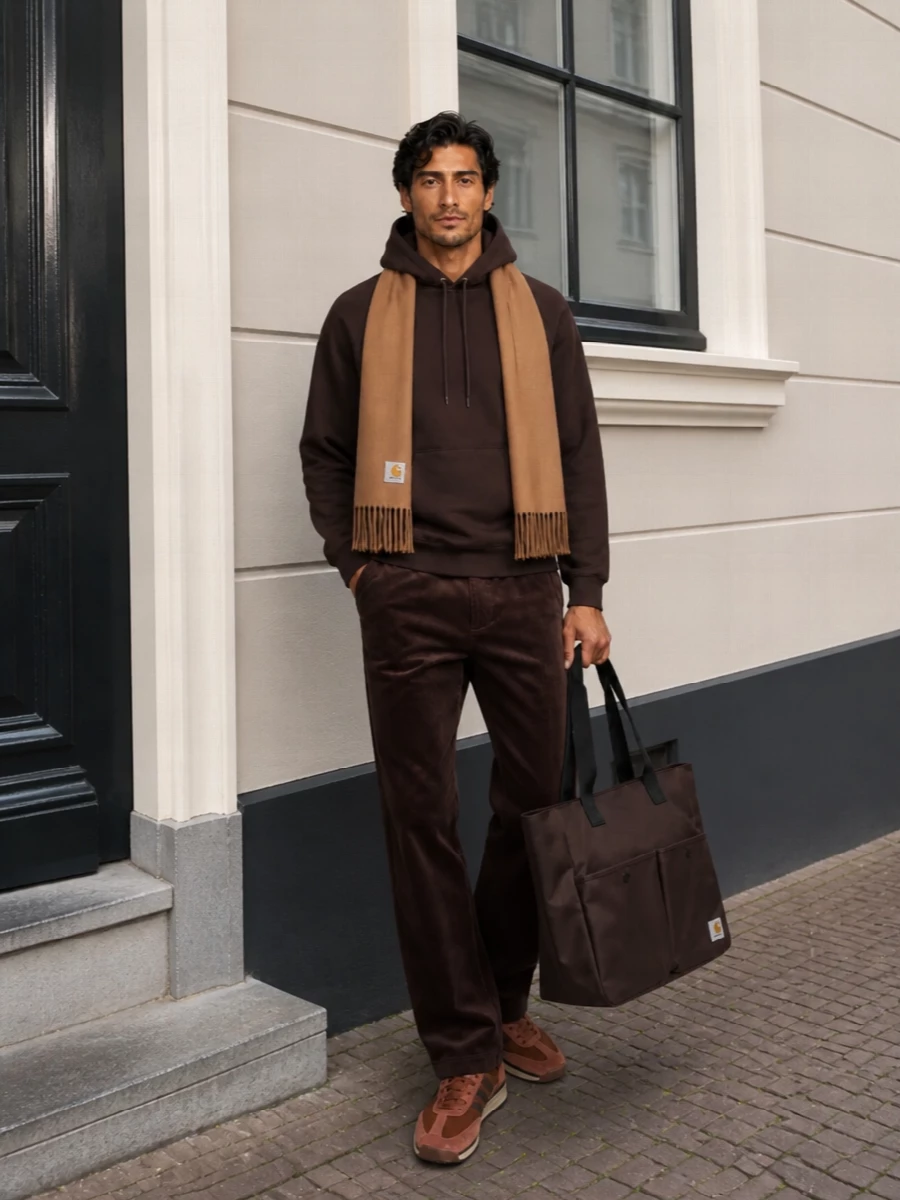 Deep brown on brown gives this Carhartt WIP uniform a quiet, utilitarian weight, with cord texture breaking up the hoodie’s clean fleece. Rust suede runners keep it grounded in streetwear rather than pure workwear, while the oversized dark tote and camel scarf make it feel ready for long city days in cold weather. The result is relaxed, tonal and practical without losing attitude.