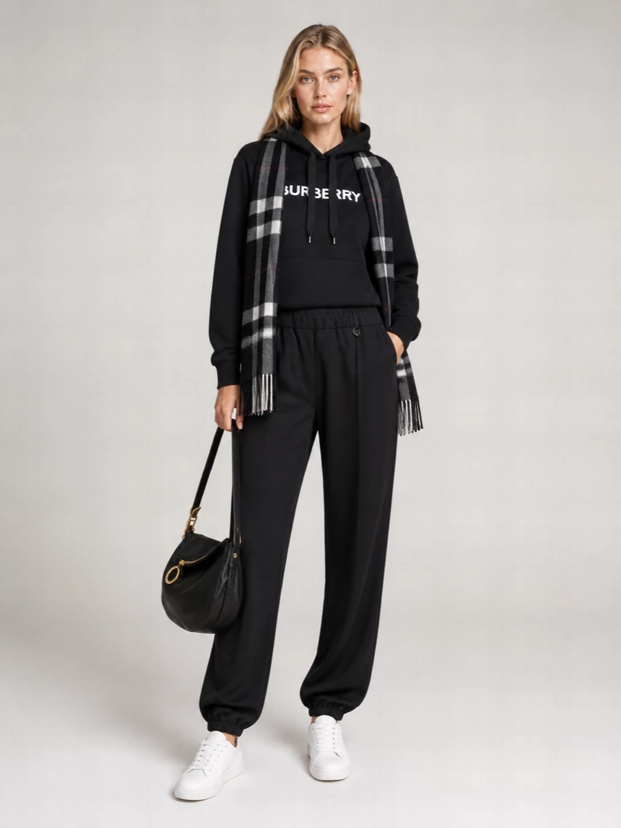Monochrome and quietly branded, this set takes the black Burberry hoodie into a streamlined head-to-toe lounge uniform. Fluid joggers and crisp white sneakers keep the mood soft yet sharp, while the slouchy crescent bag and checked scarf add just enough structure for city errands or long-haul travel. It is relaxed comfort, handled with real precision in proportion and detail.