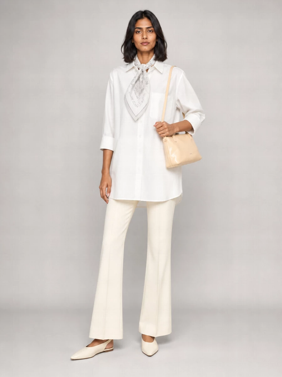 Soft white tailoring, cut long and clean, is grounded with a high-rise ivory flare to create an unbroken column that feels calm but assured. A sharp cream slingback and glossy butter-toned shoulder bag bring just enough definition, while a sketch-like silk scarf adds a quiet, intellectual accent within the same restrained palette.