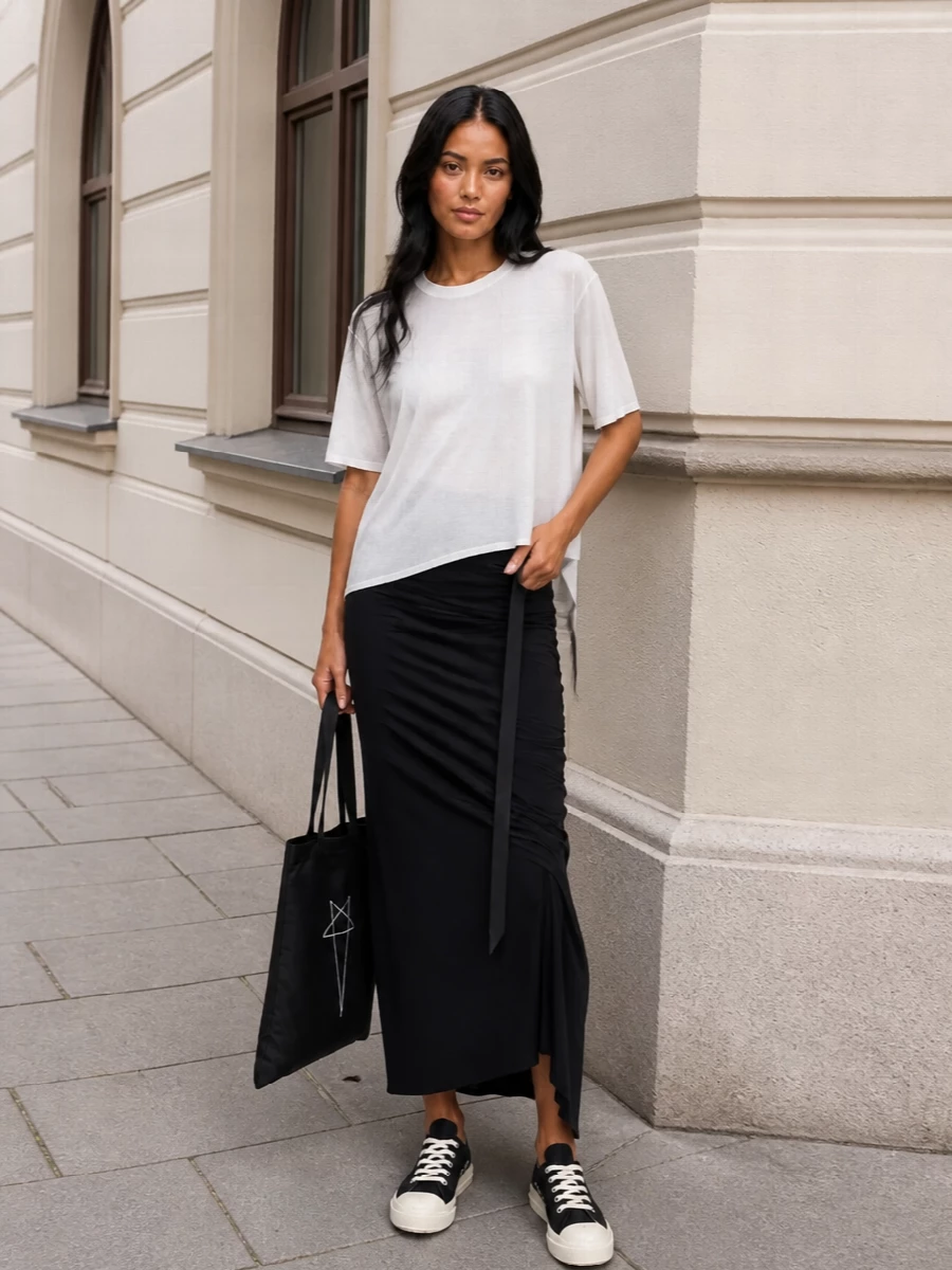 The soft white asymmetric DRKSHDW tee sits against a fluid black ruched maxi skirt to create a long, graphic column that feels unmistakably Rick yet easy for SS. Black DRKSHDW low-top sneakers and the elongated black tote keep the palette tight and urban, grounding the semi-sheer jersey in a practical, street-led silhouette that still reads quietly subversive. It's a head-to-toe Rick uniform that’s effortless by day and moody enough for late-night gallery runs.