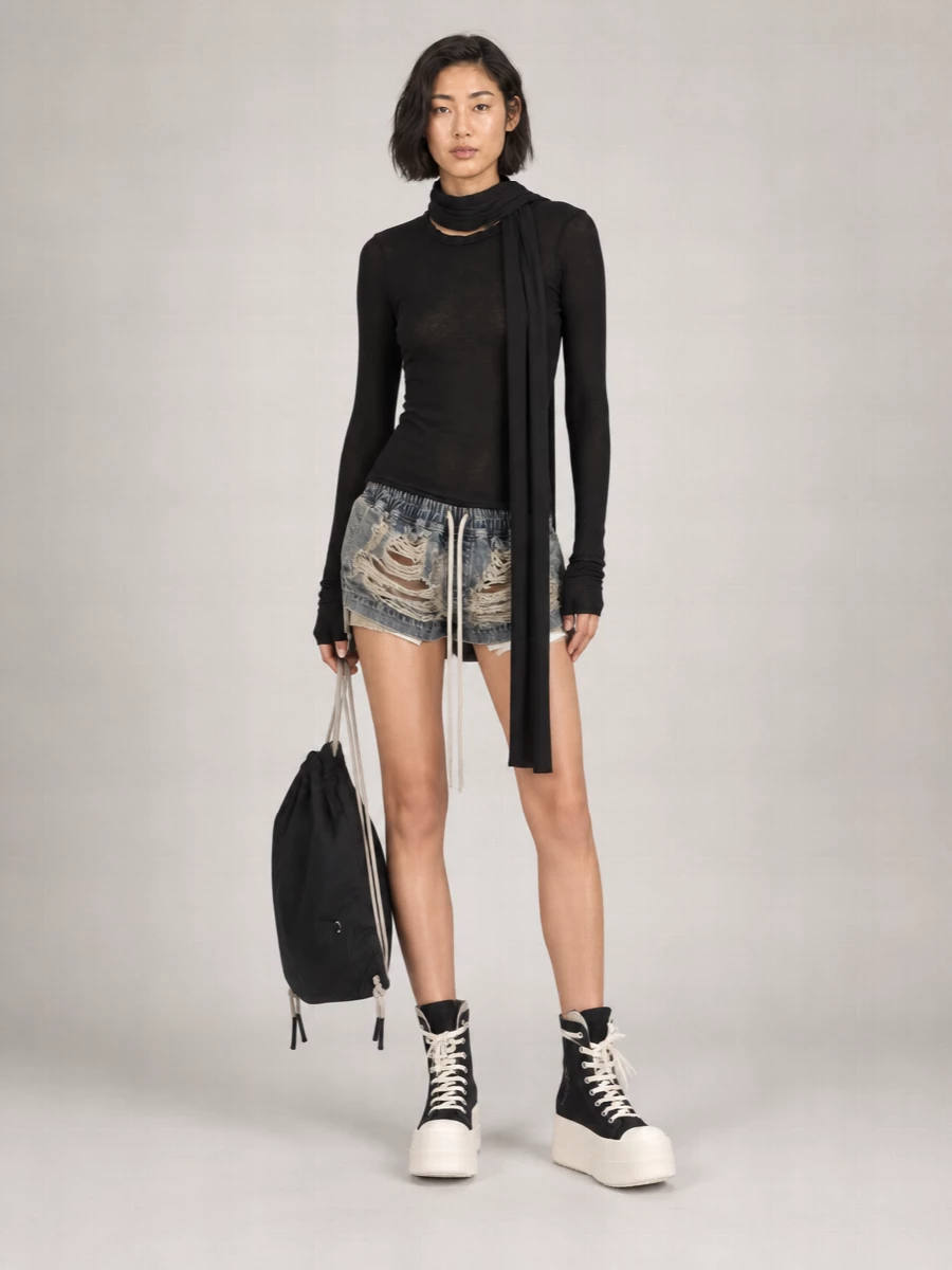 This is a dark, off-duty Rick Owens uniform built around shredded denim shorts and a second-skin black knit, all in a tight, muted palette. Chunky platform high-tops and a flat drawstring sack keep the proportions graphic and utilitarian, while the long scarf adds movement and depth. The result is slouchy, directional streetwear that feels considered from every angle, even when it is barely there on the leg.
