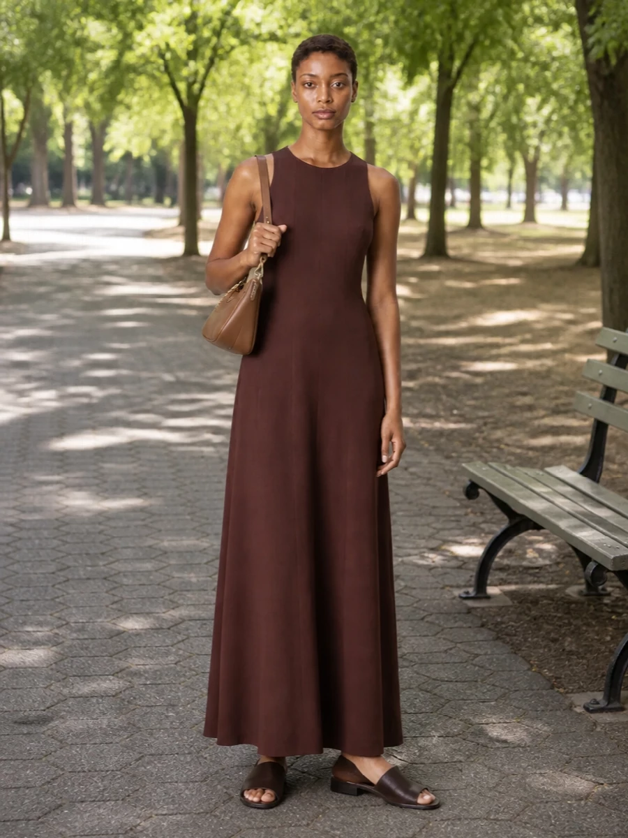 A single sweep of chocolate brown creates an elongated, understated base that lets the Prada caramel shoulder bag read as a refined highlight rather than a statement. The fluid maxi line and flat slides keep it city-appropriate yet relaxed, ideal when you want polish that feels completely unforced. Choosing the dress route over separates here preserves that uninterrupted column and keeps the palette quietly tonal around the bag’s warm leather and gold hardware.