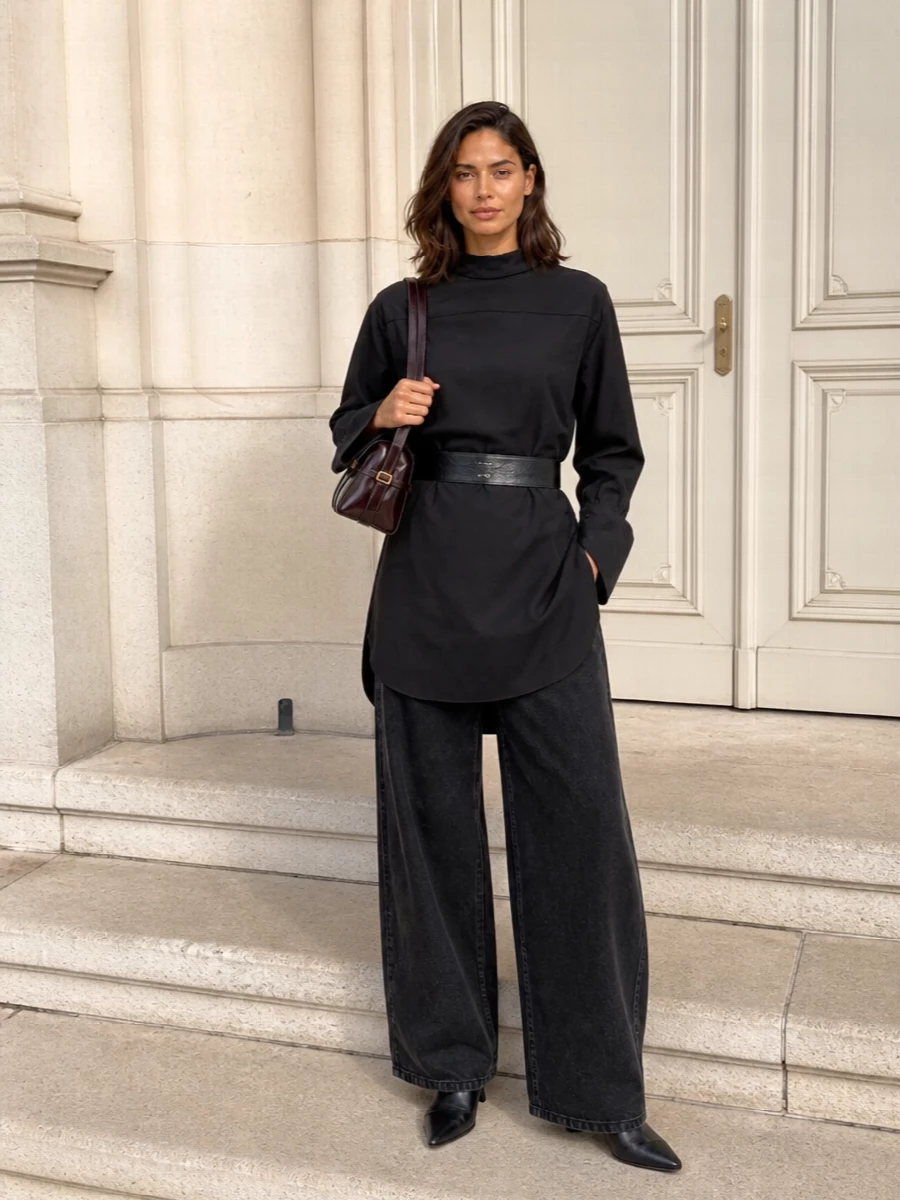 A long black Dries shirt falls over washed black wide-leg trousers to create a precise, monochrome column that feels considered rather than severe. Sculpted black ankle boots keep the lines sharp without shouting, while the oxblood shoulder bag and a discreet designer belt introduce depth through texture and tone. It is an easy uniform for city days that move straight into dinner, all in the same quiet vocabulary.