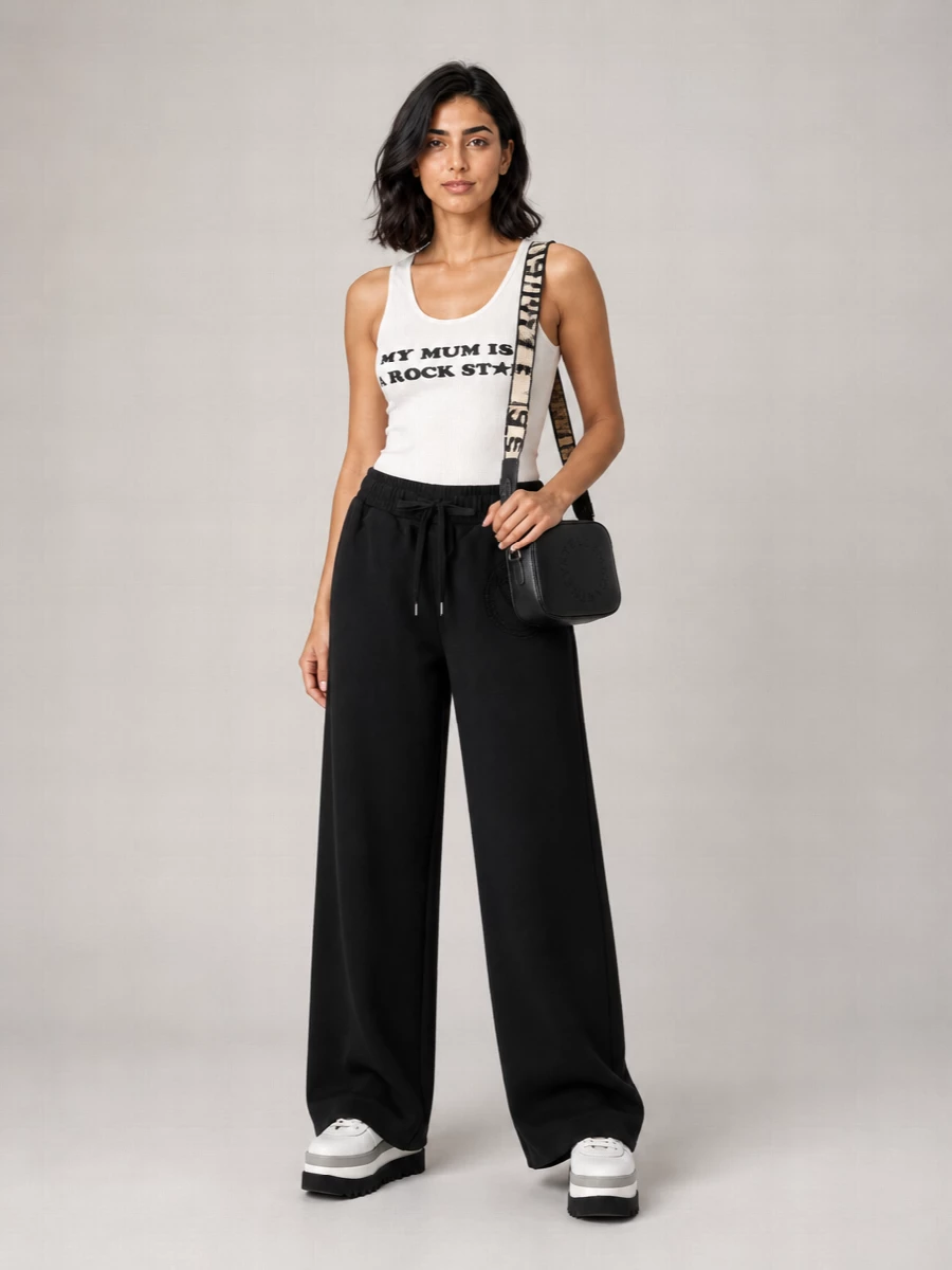 A graphic ribbed tank meets high-rise black wide-leg joggers for an easy, elongated take on off-duty streetwear. Chunky white platform sneakers pick up the print while adding height, and a compact black crossbody keeps the whole pairing sharp and streamlined. Monochrome and quietly bold, it is built for coffee runs, flights and city days on repeat.