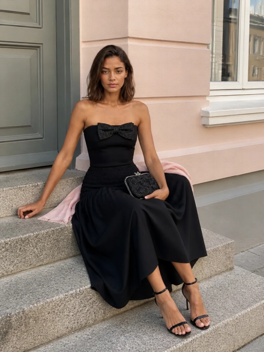 An all-black Self-Portrait ensemble that lets proportion and texture do the work: a sculpted, crystal-bow top cinching the torso above a full, smocked-waist maxi skirt. Bare ankles and a slim stiletto keep the line light, while the embellished clutch adds just enough shimmer for dinner, gallery openings and late drinks. It is polished, romantic and quietly theatrical without feeling fussy.