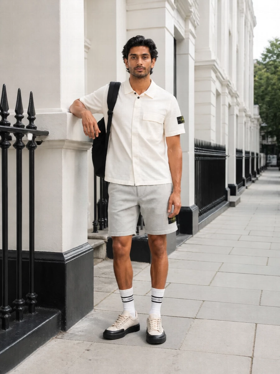 A light, technical Stone Island set built around soft neutrals and clean lines, this pairing keeps the focus on easy movement and subtle branding. The off-white shirt and pale grey shorts sit in the same calm register, while the neutral runners and black backpack sharpen the street edge without tipping the outfit into heavy contrast. It is relaxed enough for warm days in the city yet considered from every angle.