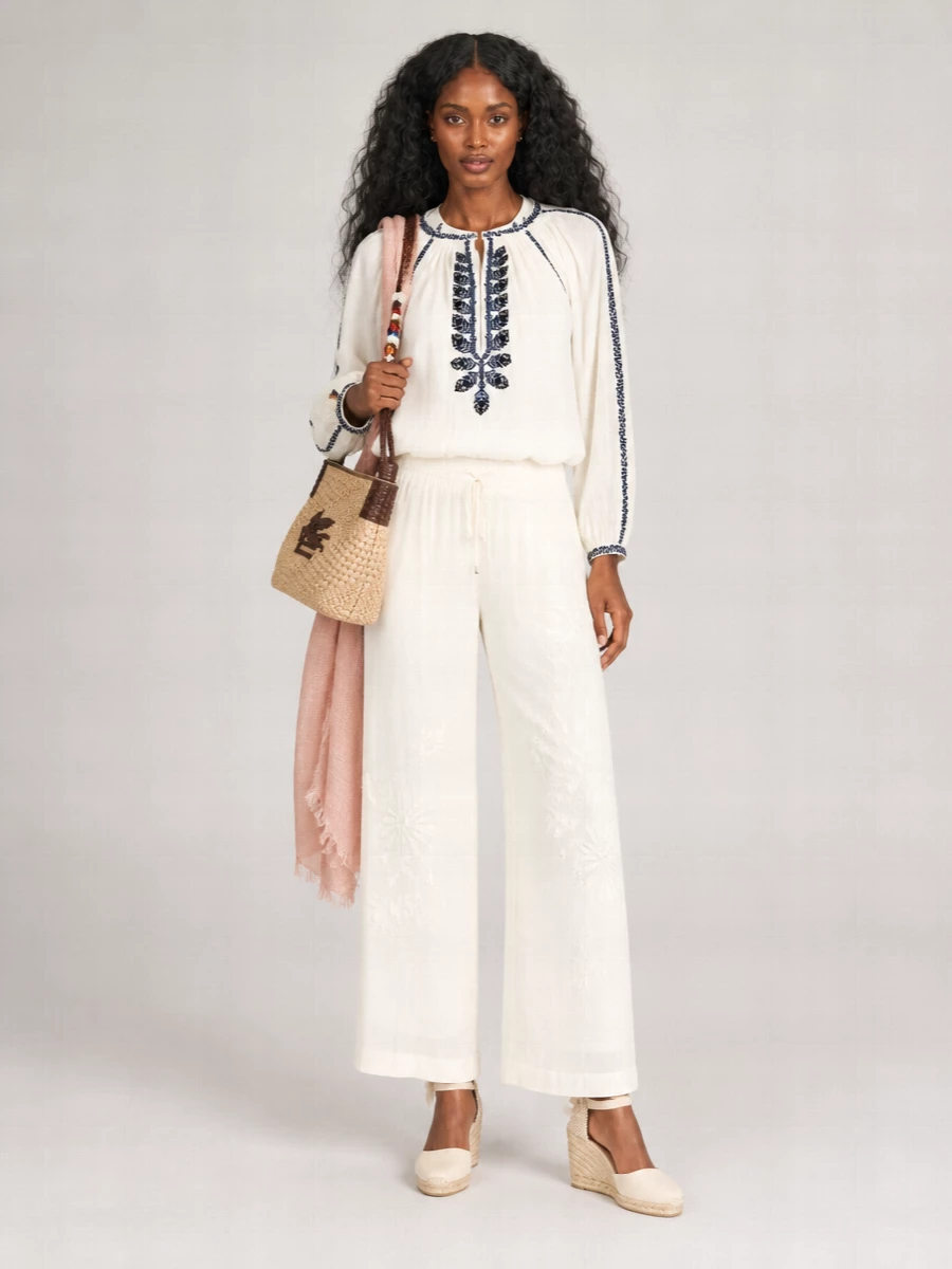 Soft ivory and navy embroidery meet fluid ivory trousers for a romantic, sun-ready outfit that feels relaxed but considered. The high waist and wide leg create a long, easy column, while the woven raffia shoulder bag and ivory wedges keep everything grounded in warm-weather boho charm. A blush scarf introduces just enough color for a quietly feminine finish.