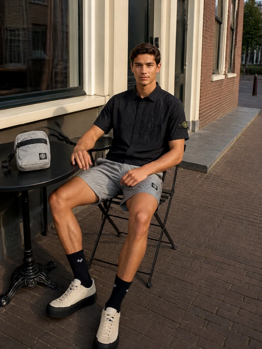 A monochrome, technical Stone Island story built around crinkled grey shorts and a black nylon shirt, this outfit feels precise but easy for city heat. Cream and sand runners soften the palette while still reading sporty, and a matching grey crossbody keeps everything hands-free and streamlined. Wear it for days when you want real function with a very clear point of view.