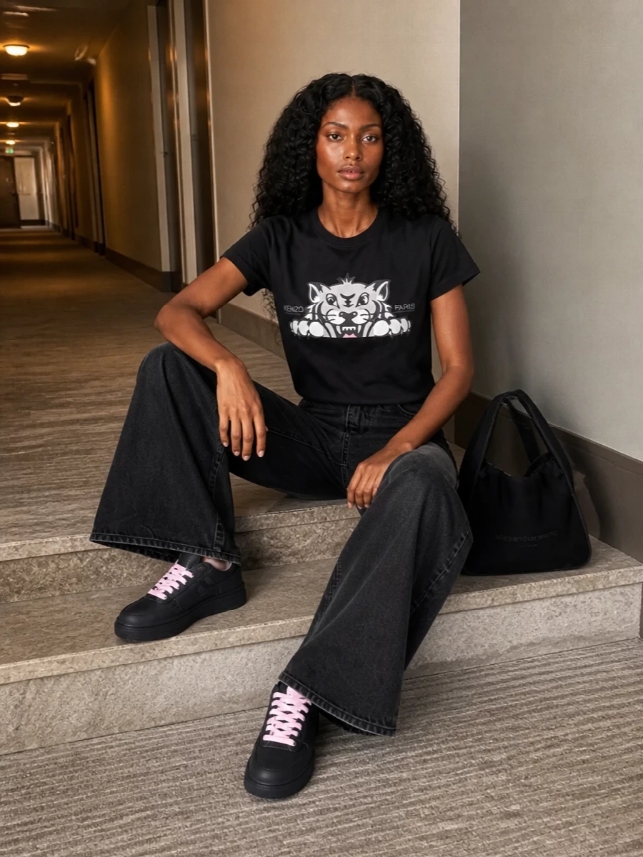 Kenzo’s reworked tiger tee pairs with the brand’s washed‑black wide‑leg denim for a clean, graphic take on streetwear that still feels relaxed. Black satin Nikes with pink laces and blush‑accent Marni socks echo the tee’s soft colour hit without breaking the monochrome base. A quietly branded Alexander Wang shoulder bag finishes it with a polished, city-ready edge you can wear from coffee runs to late casual dinners.