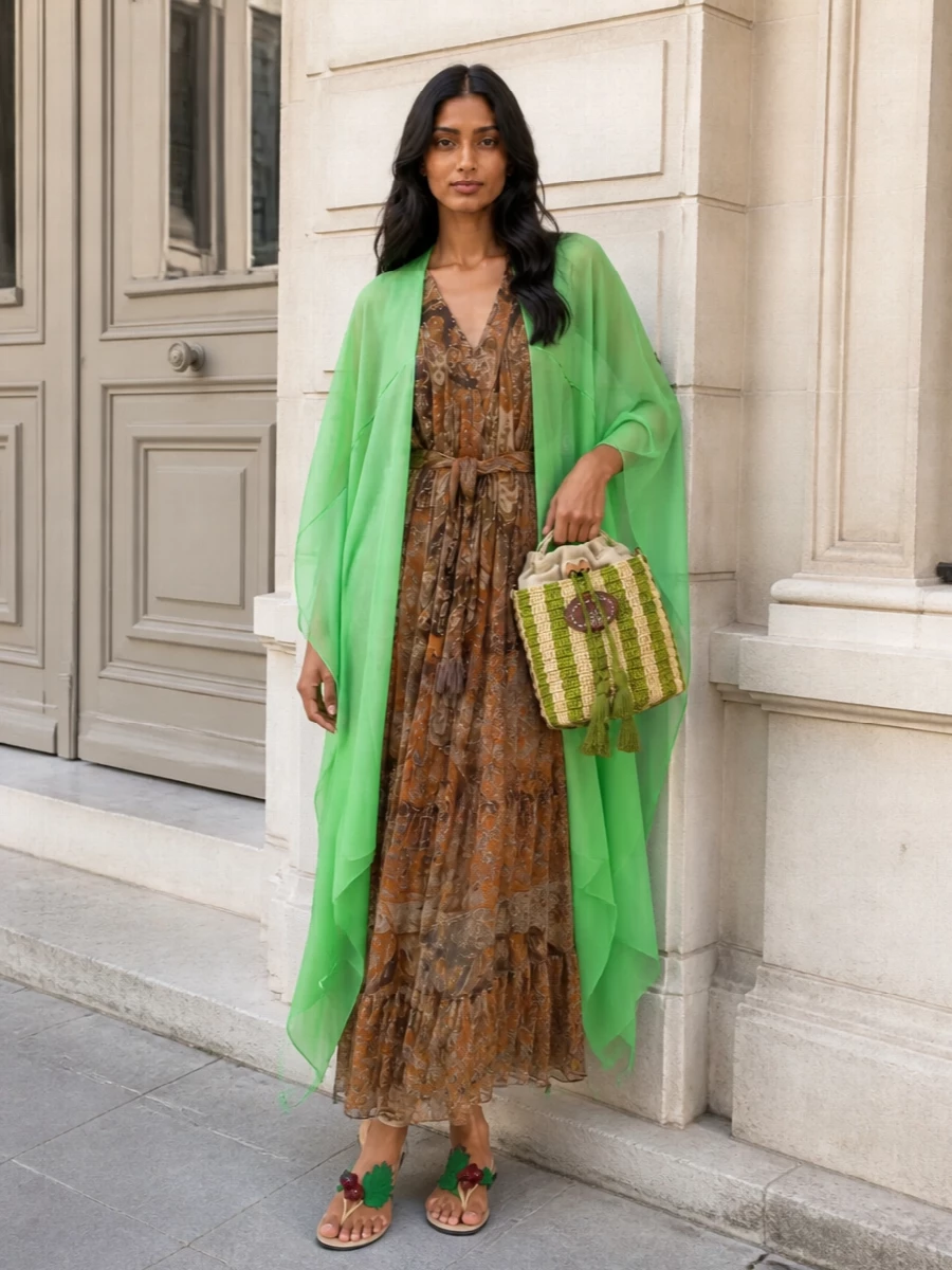 I’m styling the Dries Van Noten poncho as a sculptural layer over the Zimmermann paisley wrap dress, so the body is grounded in warm, earthy romance while the green chiffon reads as a luminous veil. Valentino’s leaf-wrapped sandals and raffia bucket echo the poncho’s color and movement, turning the whole into a quietly theatrical garden-party ensemble that can slip from terrace cocktails to seaside dinners without feeling costume-y. The proportions stay long and fluid throughout, so all that transparency feels intentional rather than busy.