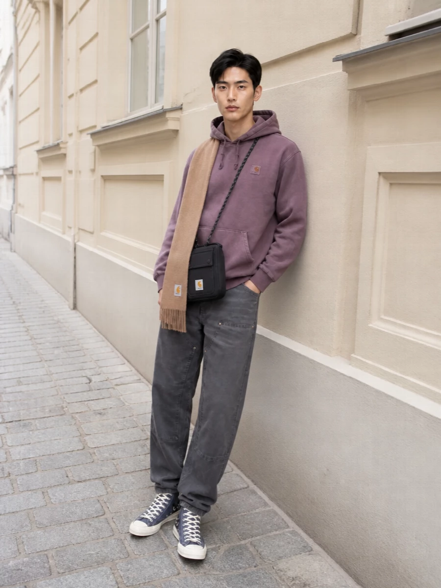 Dusty mauve and washed charcoal do the work here, giving classic Carhartt shapes a softer, worn-in edge that still feels purposeful. The straight-leg work pant and high-top stack keep proportions relaxed but sharp, while the compact crossbody and camel scarf bring just enough function and warmth for cold city days.