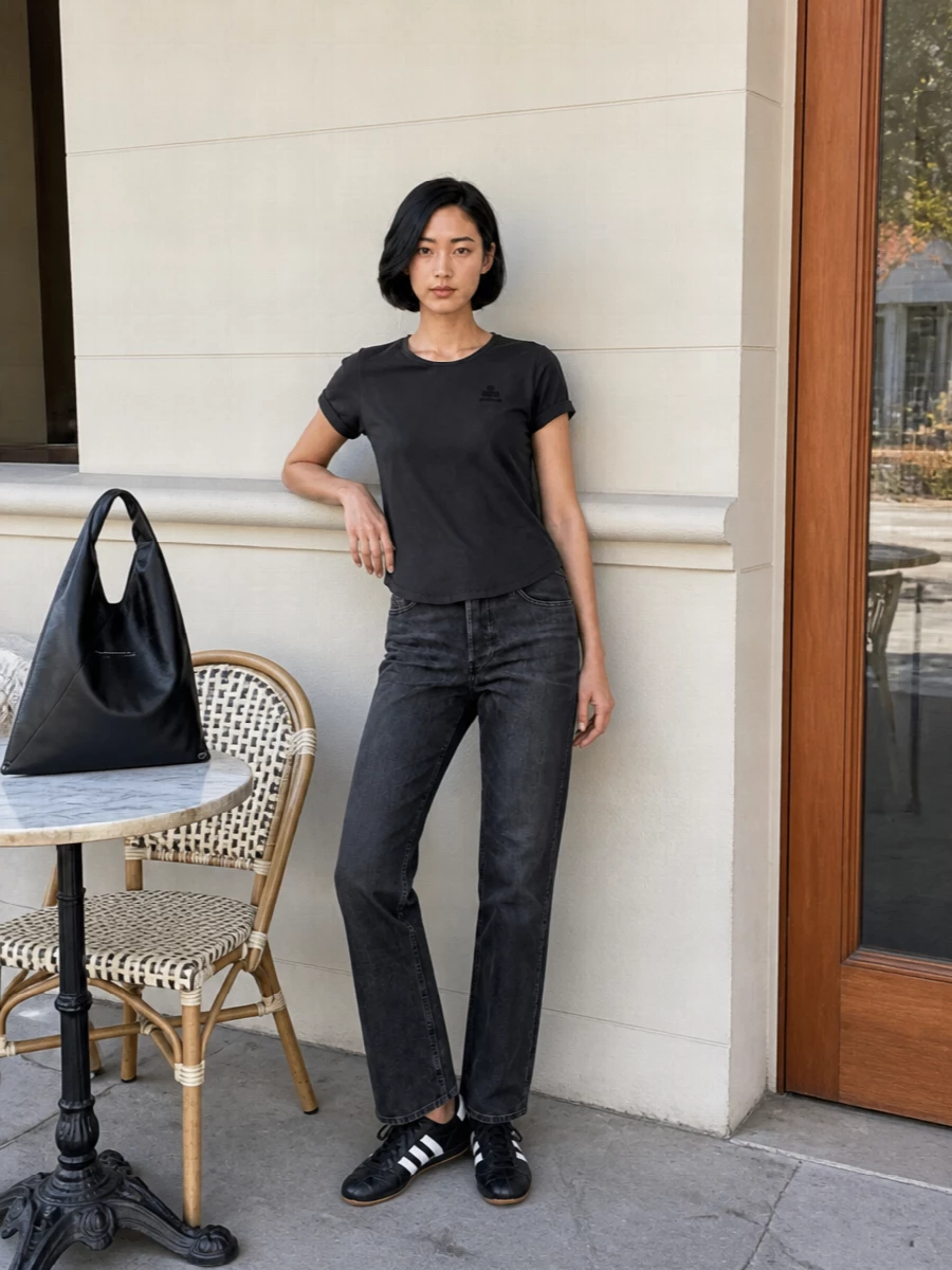 Washed charcoal denim with a softly faded black tee creates a tight, monochrome base that feels relaxed but deliberate. Black and white terrace sneakers keep it grounded and agile, while the sculptural Margiela tote adds just enough edge to carry you from errands to evenings out without changing a thing.