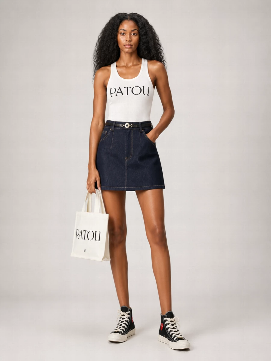 Patou’s ribbed logo tank meets its match in a structured dark-indigo A-line mini for a clean, Parisian take on off-duty dressing. Graphic black high-tops and a petite logo canvas tote keep the palette tight and casual, while a slim belt defines the waist so the proportions feel intentional rather than sweet.