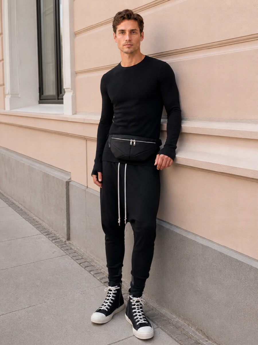 An all-black Rick uniform that stretches the torso with a second-skin knit, then drops cleanly into relaxed, tapered volume through the leg. Contrast drawstrings and canvas high-tops echo each other, giving the proportions a deliberate, graphic rhythm while the belt bag sits close so the silhouette stays long and unbroken.