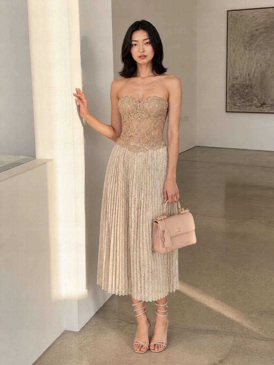 A sculpted nude lace corset meets a fluid champagne pleated midi, creating a column of warm light that feels sensual yet composed for summer evenings. Crystal-wrapped sandals and a blush top-handle bag continue the soft, luminous palette, so the focus stays on texture and line rather than loud contrast. The result is romantic, formal and quietly decadent, perfect for weddings, terrace cocktails or any after-dark occasion where you want couture-level detail to whisper rather than shout.