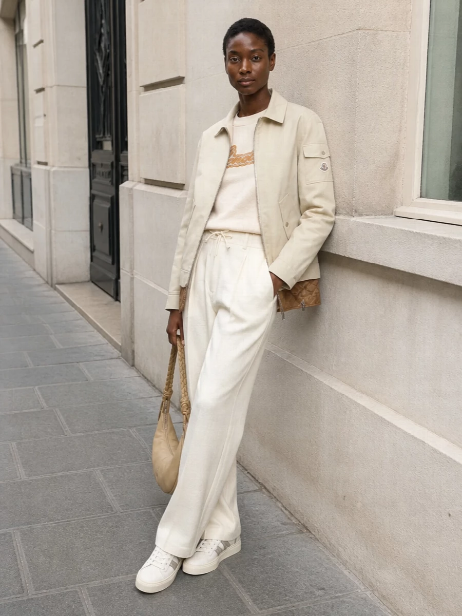I’ve anchored the look around the TOP + BOTTOM route rather than a dress so the Moncler jacket can sit naturally within a layered, aprè‑s ski‑meets‑city uniform in soft neutrals. The buttercream logo sweatshirt and fluid ivory wide‑leg trousers echo the jacket’s beige and caramel, while off‑white sneakers and a sand crescent bag keep everything light, minimalist and quietly polished for FW travel or relaxed city days. The silhouette stays clean and elongating, with just enough volume in the trouser to balance the hip‑length outerwear without feeling oversized.