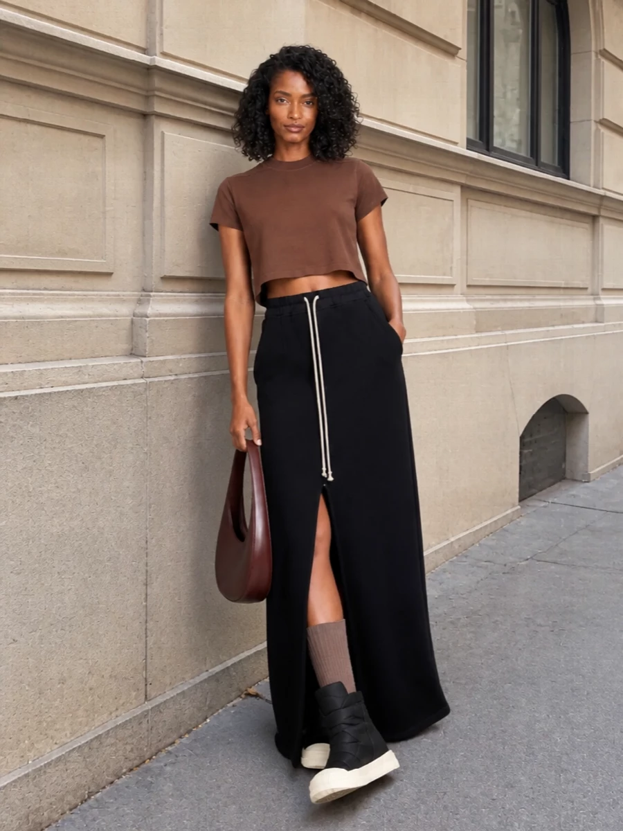 This look builds a dark, elongated Rick Owens DRKSHDW silhouette around the cropped chocolate tee, pairing it with a high-waisted black sweat maxi that pools over graphic platform boots. The deep-brown sculptural Coperni bag and tonal knee-highs keep the palette in the brown–black spectrum, delivering a quietly subversive FW uniform that feels minimal, urban and intentionally architectural.
