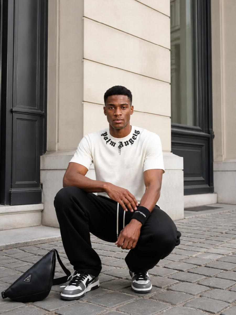 A clean monochrome street set that lets the Gothic neckline do the talking, grounded by relaxed black track pants and graphic court sneakers. The wide leg and boxy tee create an easy skate silhouette, sharpened slightly by the structured crossbody. It is low-effort, logo-forward dressing that still reads considered from afternoon runs to late-night city walks.