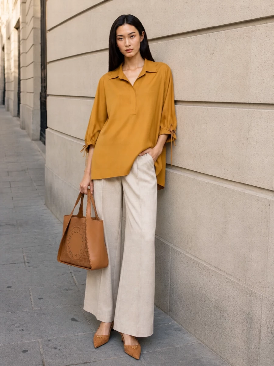 A mustard Max Mara tunic skims over light-beige high-waisted wide-leg trousers for an elongated, quietly luxurious silhouette in soft, sunlit neutrals. Tan woven Prada kitten-heel slingbacks and a structured caramel Stella tote pick up the warm tones, adding subtle texture and polish while keeping the outfit effortless for city days and terrace evenings alike.