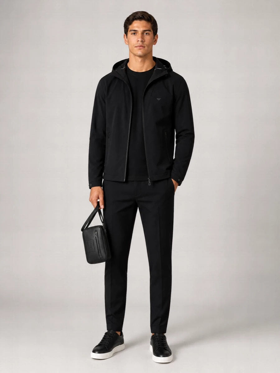 A monochrome Emporio Armani set that treats technical city wear with a quiet, precise hand. The clean tee, tailored track pant and grained leather sneaker sit neatly under the hooded shell, while a compact crossbody keeps the line sharp and functional. It is made for urban days that move from commute to coffee to late walk home without a change of gear.