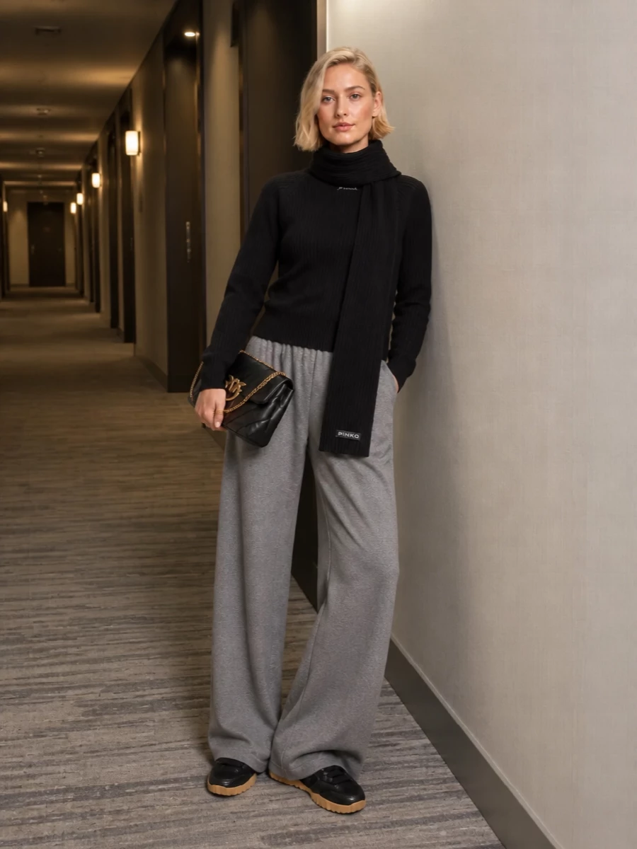 An all-knit, monochrome base keeps this outfit calm and considered, with the black ribbed sweatshirt cleanly topping the fluid heather grey wide-leg trouser. Chunky black sneakers with a gum sole ground the volume, while the quilted chain-strap bag and matching ribbed scarf add just enough texture and structure for city days that run long.