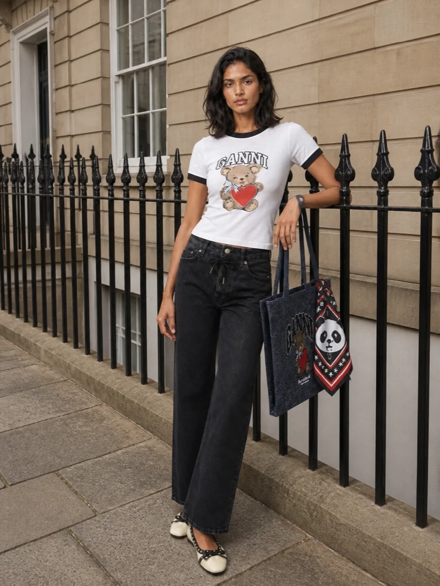 Ganni’s teddy tee meets washed black denim for an easy city uniform that feels playful but not loud. Cream and black ballerinas echo the graphic contrast, keeping everything neat and a little punky. The indigo teddy tote and logo scarf double down on the mascot story so the whole outfit reads like a considered, tongue in cheek take on preppy streetwear.