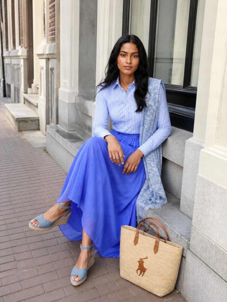 Crisp Riviera prep meets soft romance in this pairing of a striped sky-blue shirt with the flowing cobalt maxi skirt. Wedge espadrilles and a woven straw tote keep it sun-ready and relaxed, while the airy scarf in tonal blues adds a quietly bohemian finish. Ideal for coastal weekends or city afternoons when you want polish without stiffness.