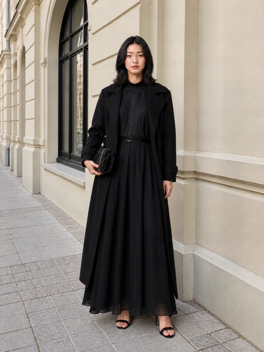 A floor-sweeping black column gown is paired with barely-there black stiletto sandals and a sculpted black clutch for a monochrome evening statement. The result is fluid, candlelit drama with quietly precise accessories that disappear just enough to let the dress move and speak.