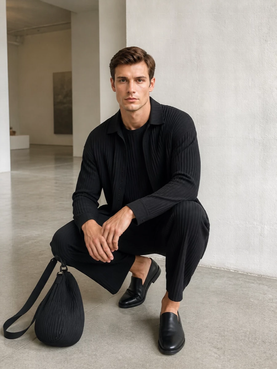 An all-black Homme Plissé story that plays with pleated texture and controlled volume, anchored by a crisp slip-on loafer. The cropped wide leg and regular shirt-jacket frame a clean pleated tee, while the sculptural crossbody echoes the same architectural rhythm. It is precise, quiet and designed for days that slide easily into understated evenings.